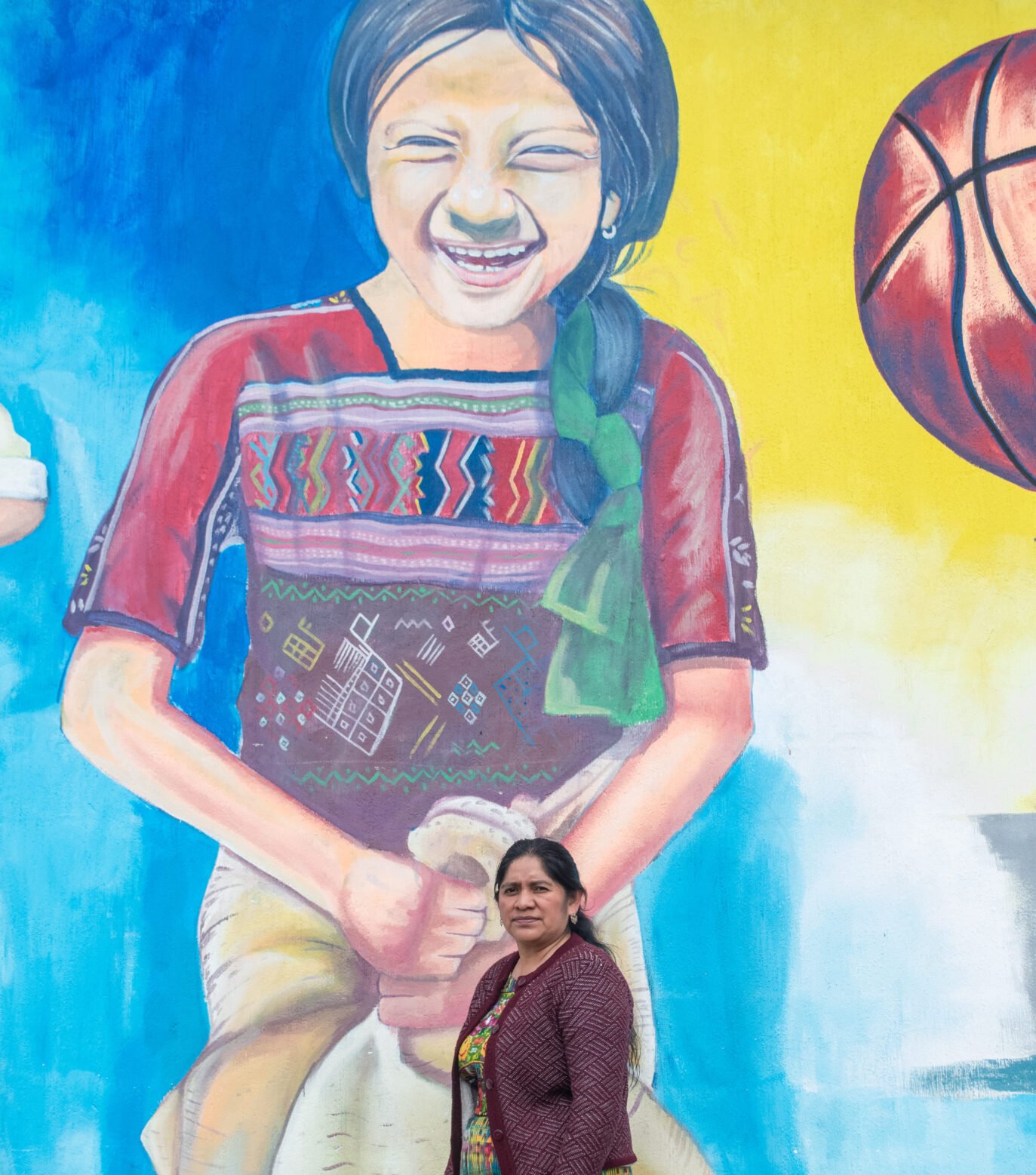  Una niña sonriendo con su indumentaria maya Kaqchikel, plasmada en un mural, destaca el trabajo de Ester Miza en San Juan Comalapa. 