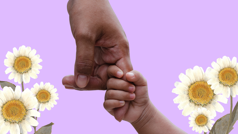 Mano de bebé tomando el dedo de una mano adulta. Hay flores al fondo.